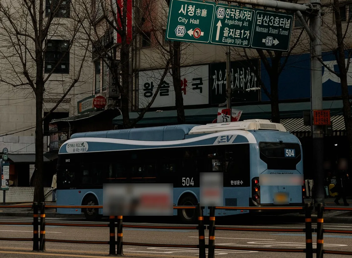 한글 도로 안내 표지 아래 서울 도심 도로에 서 있는 파란색 시내버스